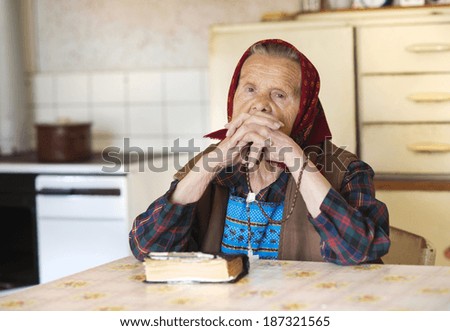 Very old woman wearing head scarf is praying in her country style kitchen