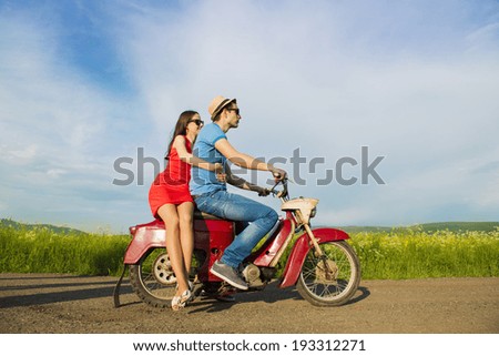 Happy young couple in love on retro motorbike driving togetger and ejoying the trip in green field