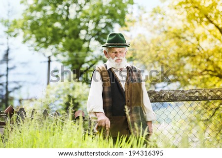 Old farmer with beard and hat is walking in his back yard