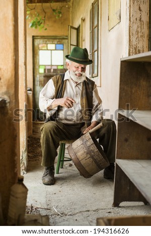 Old farmer with beard and hat is working by his farmhouse
