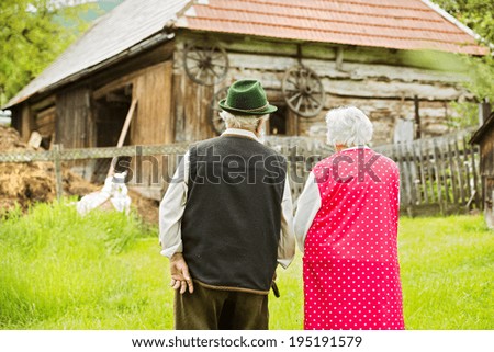 Rear view of old farmers couple standing by their farmhouse