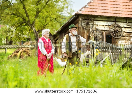 Outdoor portrait of old farmers couple standing by their farmhouse