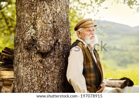 Old farmer with beard is walking in meadow