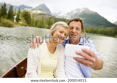 Senior couple on boat with mountains in background taking selfie