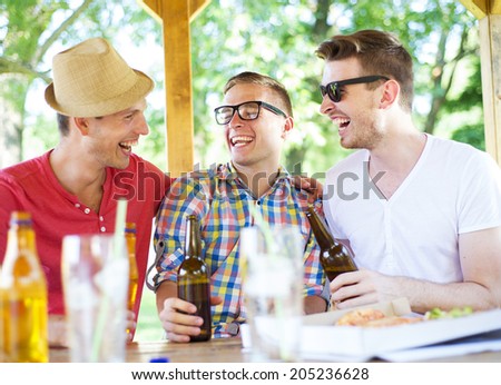 Three happy friends drinking beer, chatting and having fun in pub garden