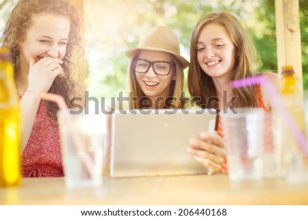 Three beautiful girls drinking and having fun with tablet in pub garden