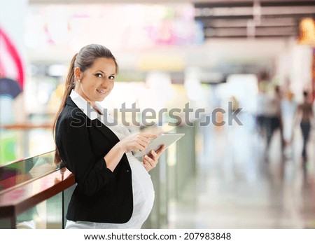 Busy pregnant woman using tablet in shopping mall
