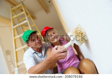 Active senior couple painting wall with brush in new house. They are having fun.