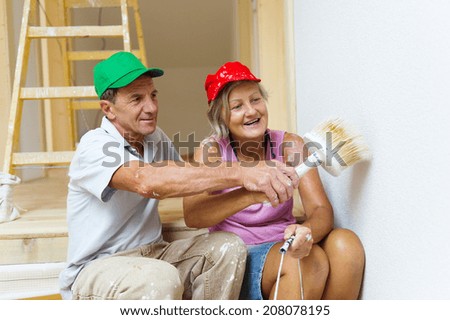Active senior couple painting wall with brush in new house. They are having fun.