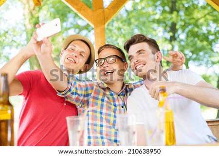 Three happy friends drinking and taking selfie with smartphone in pub garden