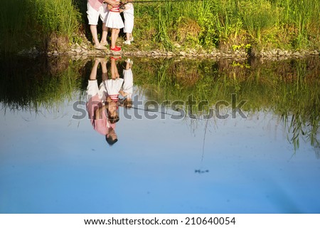 Happy young father fishing on the lake with his little daughters, reflecting in the water