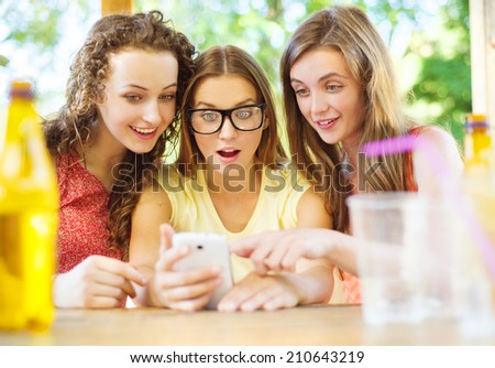 Three beautiful girls drinking and having fun with smartphone in pub garden