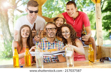 Group of happy friends drinking and eating pizza in pub garden