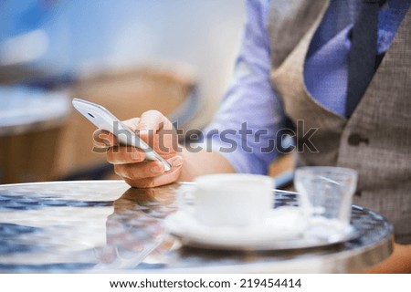 Detail of businessman drinking espresso coffee in the city cafe during lunch time and using mobile phone