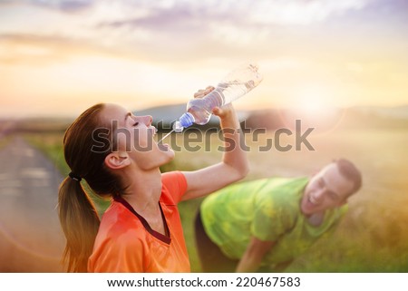 Cross-country trail running couple having water break at sunset