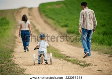 Happy family with little boy on wooden tricycle walking in ntaure