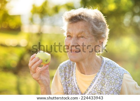 Portrait of senior woman in apron eating apple in the sunny garden