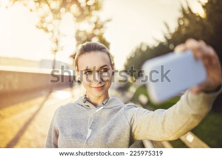 Young female runner is having break and taking selfie during the run in city on a quay