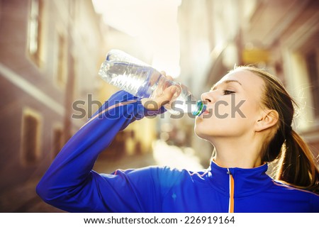 Young female runner is having break, drinking water during the run in city center