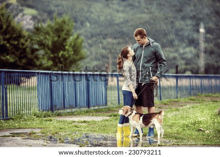 Young couple in colorful wellies walk beagle dog in rain.