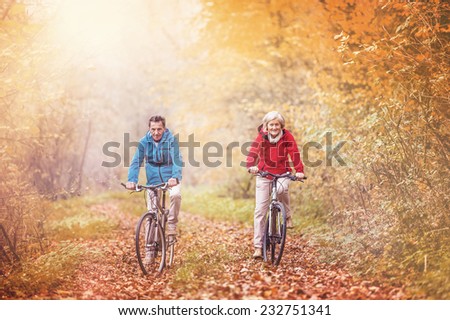 Active seniors ridding bike in autumn nature. They relax outdoor.