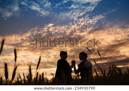 Love couple in sunset field. They wearing traditional Eastern Europe folk costumes.