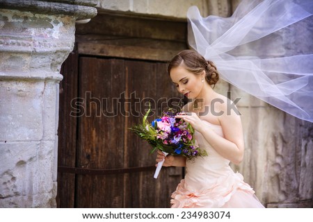 Beautiful bride in veil standing by the old stone chapel.