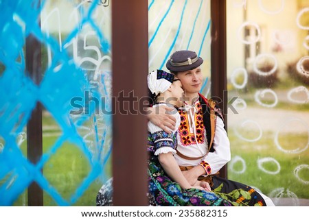 Love couple wearing traditional Eastern Europe folk costumes sitting at the bus stop.