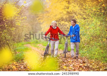 Active seniors having walk with bike in autumn nature. They having romantic time outdoor.