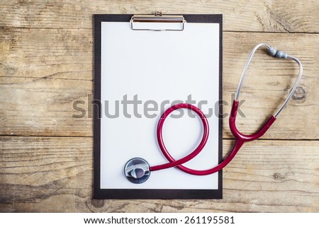 Workplace of a doctor. Stethoscope and clip board on wooden desk background.