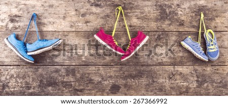 Three pairs of running shoes hang on a nail on a wooden fence background
