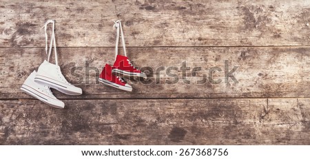 Two pairs of sports shoes hang on a nail on a wooden fence background