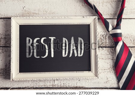 Rectangle picture frame with Best dad sign and colorful tie laid on wooden floor backround.