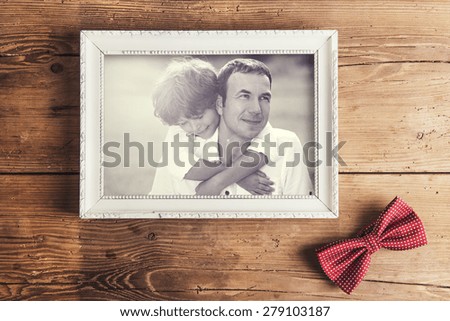 Picture frame with family photo and dotted bow tie laid on wooden backround.