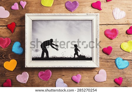 Fathers day composition - picture frame and colorful hearts on the floor. Studio shot on wooden background.