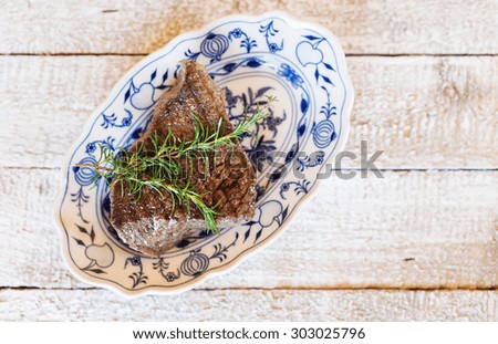 Grilled beef steak on a serving plate with fresh rosemary spring