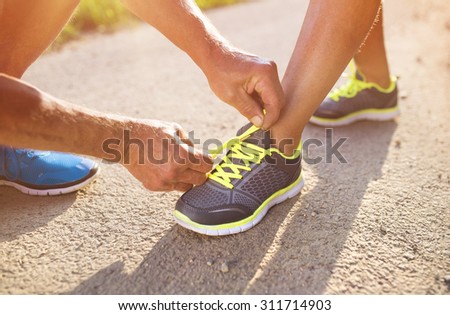 Unrecognizable seniors tying shoelaces before a run outside in green nature