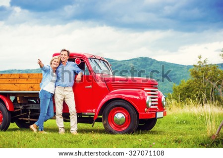 Senior couple standing by their vintage red car