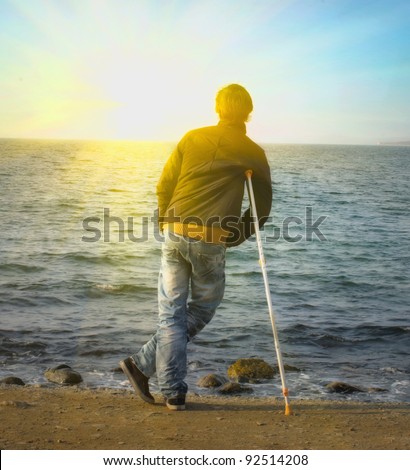 Yang man hiking on crutches on the beach