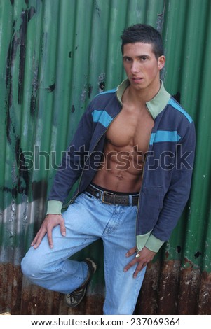 Young muscular man in an unzipped jacket in front of a green crimping metal wall.