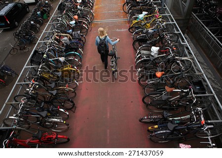 AMSTERDAM, NETHERLANDS - AUGUST 9, 2012: Woman pushes a bicycle on through the bicycle parking station next to the Central railway station in Amsterdam, Netherlands.