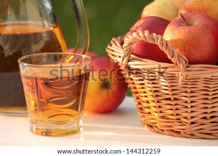 Glass with juice and basket with apples in a garden.