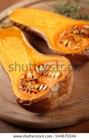 Close up of baked butternut squash and herbs on wooden board.