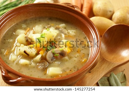 Detail of bowl with potato soup, wooden ladle and food ingredients.