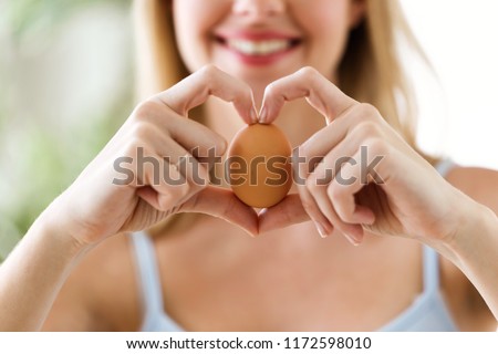 Shot of beautiful young woman showing brown chicken egg with hands in a heart shape at home. Foto stock © 