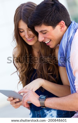 Portrait of happy young couple browsing internet with digital tablet in the street