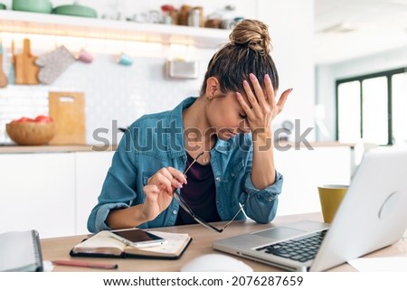 Shot of stressed business woman working from home on laptop looking worried, tired and overwhelmed int he kitchen at home.  Imagine de stoc © 