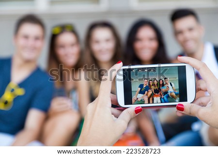 Outdoor portrait of group of friends taking photos with a smartphone in the street.