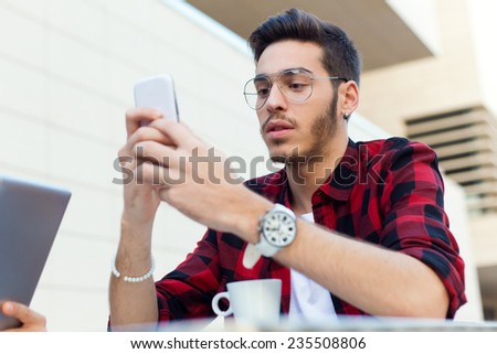 Outdoor portrait of young entrepreneur using his mobile phone at coffee shop.