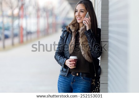 Outdoor portrait of young beautiful woman with mobile phone and coffee.